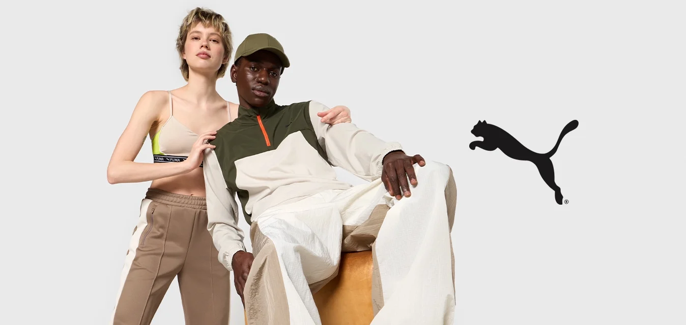 Due modelli indossano abiti casual: uno con una maglietta beige e pantaloni beige, l'altro con una maglia verde e bianca, pantaloni larghi color crema e sneakers nere.