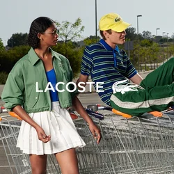 Tre persone che interagiscono con una fila di carrelli della spesa in un parcheggio vuoto, una persona sdraiata all'interno di un carrello.