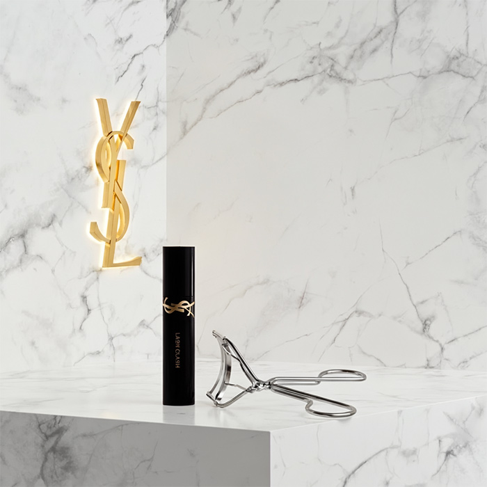 Un mascara YSL nero e un piegaciglia su una superficie di marmo bianco.