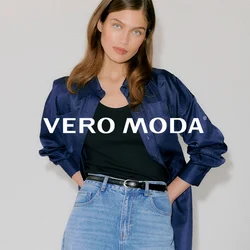 Giovane donna che indossa una camicia di raso blu scuro sopra una canottiera nera, jeans a vita alta azzurri e tacchi neri con occhielli.