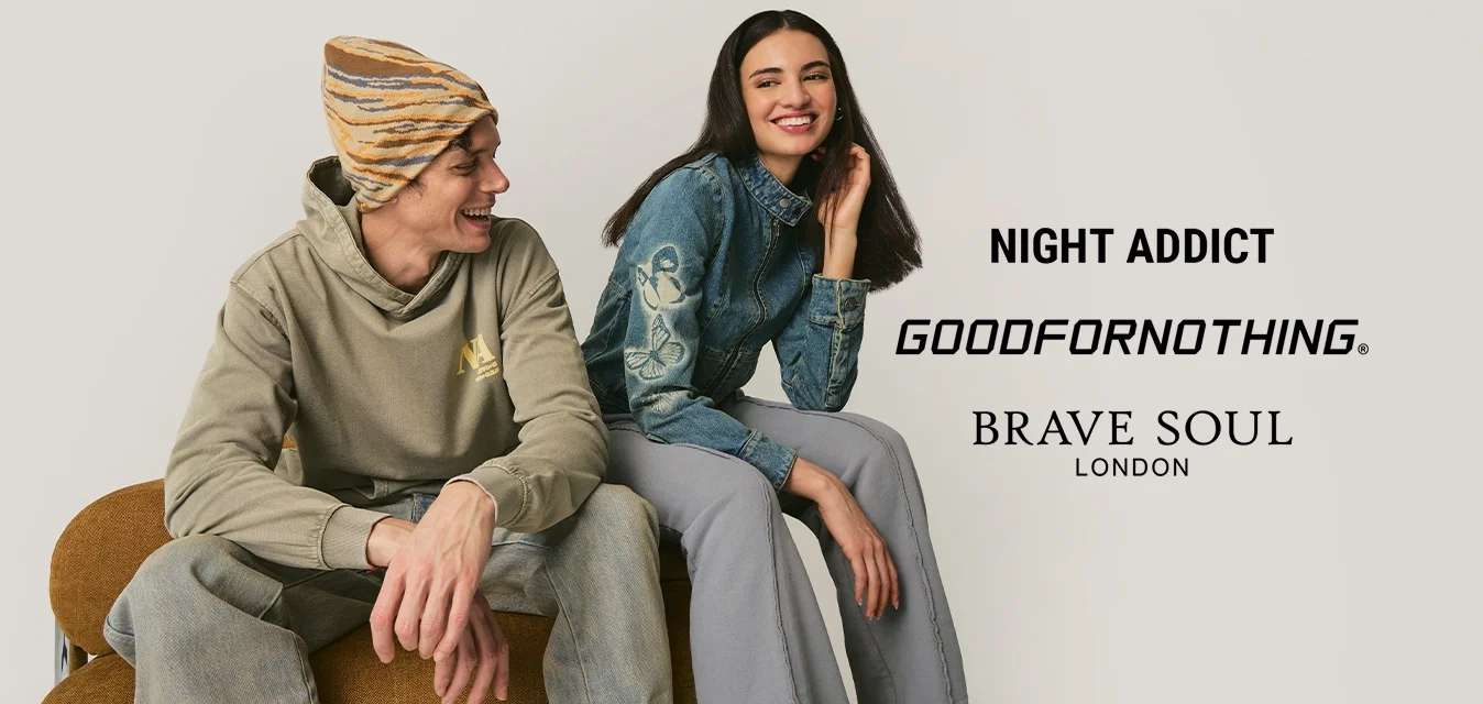 Giovane con berretto e felpa con cappuccio seduto accanto a una donna sorridente con giacca di jeans blu e pantaloni grigi su sfondo neutro.