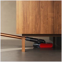 Il lavapavimenti Dyson PencilWash viene utilizzato per pulire sotto un mobile basso.