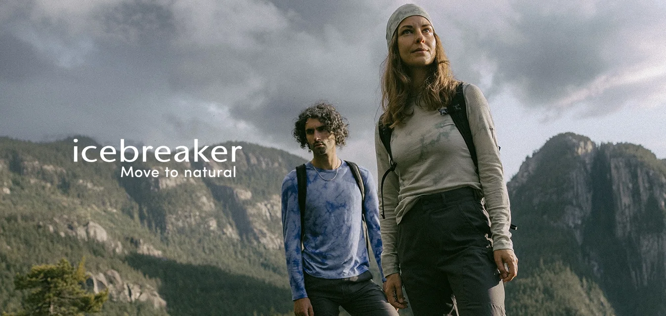 Due escursionisti si trovano su una superficie rocciosa. Uno indossa una maglietta a maniche lunghe di colore chiaro e pantaloni scuri; l'altro indossa una maglietta blu con effetto tie-dye e pantaloni scuri.