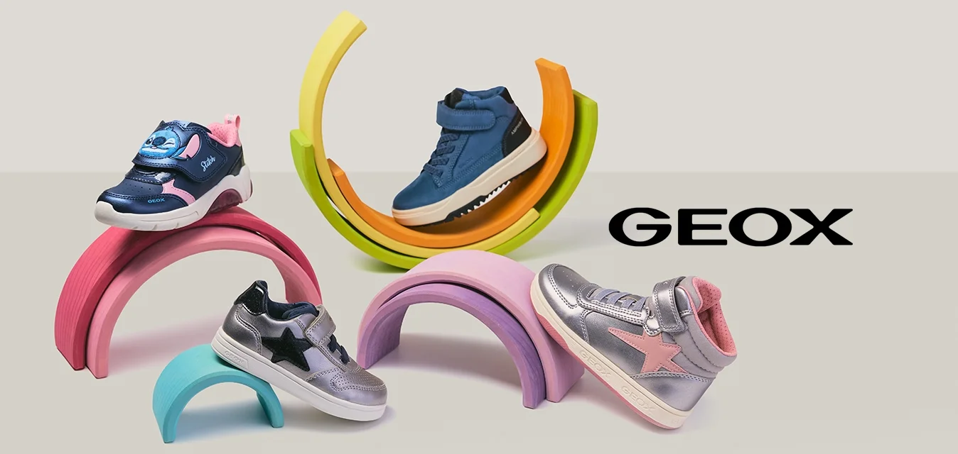 Quattro scarpe da ginnastica colorate per bambini esposte su supporti a forma di arcobaleno pastello, su uno sfondo chiaro.