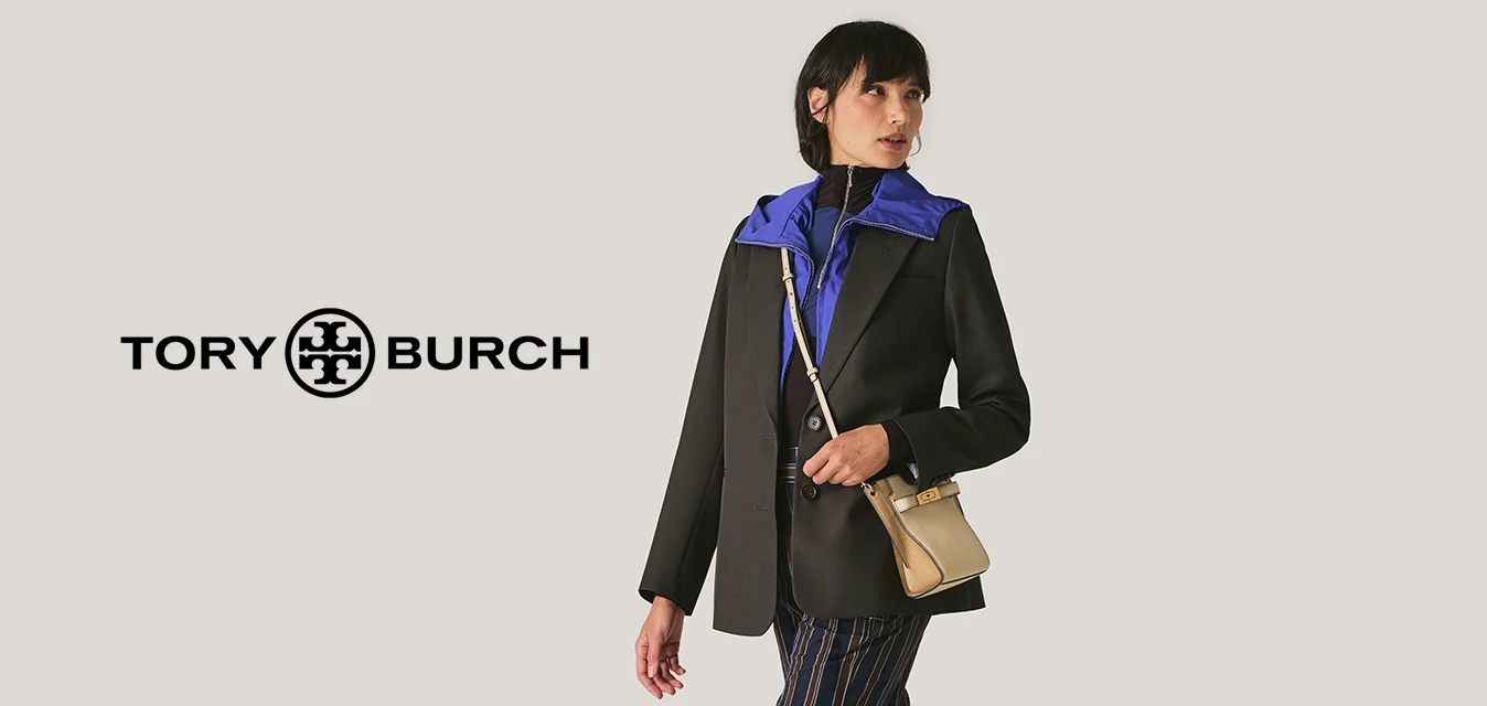 Blazer nero, top blu, pantaloni a righe, ciabatte beige pelose, piccola borsa a tracolla beige. Modella che cammina su uno sfondo chiaro.