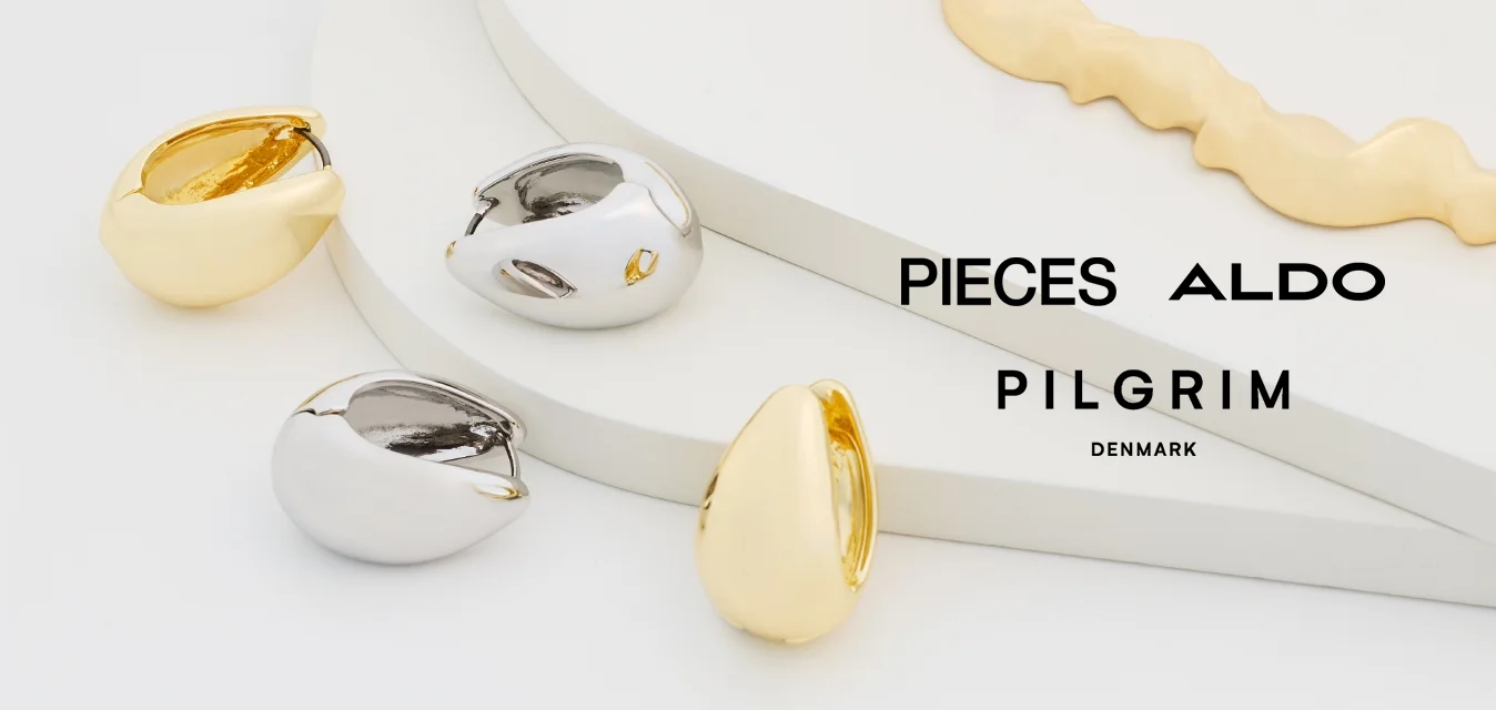 Gioielli in oro e argento esposti su uno sfondo chiaro. Tra le caratteristiche ci sono una collana in oro con texture e anelli in argento e oro con finiture lisce.