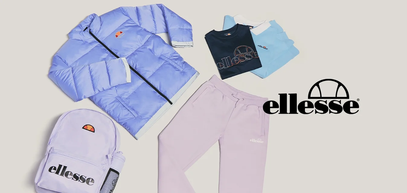 Giacca puffo viola chiaro, zaino abbinato, pantaloni jogger lilla e tre t-shirt piegate in blu navy, bianco e azzurro su sfondo beige.