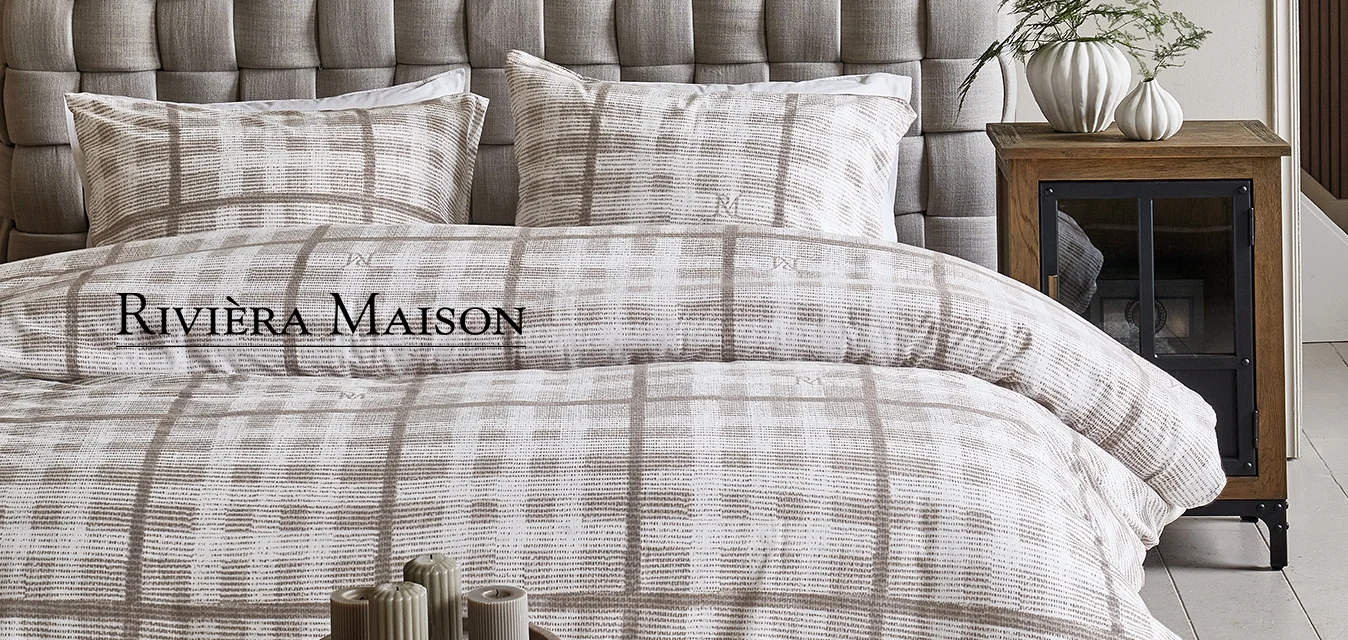 Testiera imbottita grigia con un design trapuntato, abbinata a biancheria da letto a quadri beige e bianca e cuscini decorati su un comodino in legno.