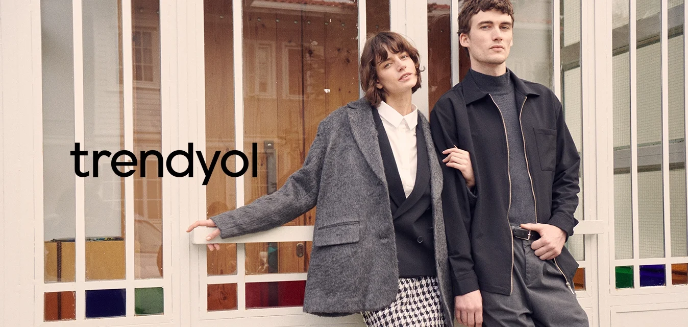 Blazer grigio oversize, camicia bianca, gonna a quadri houndstooth, calze fino al ginocchio; giacca nera con zip, pantaloni grigi; sfondo con pannelli di vetro.