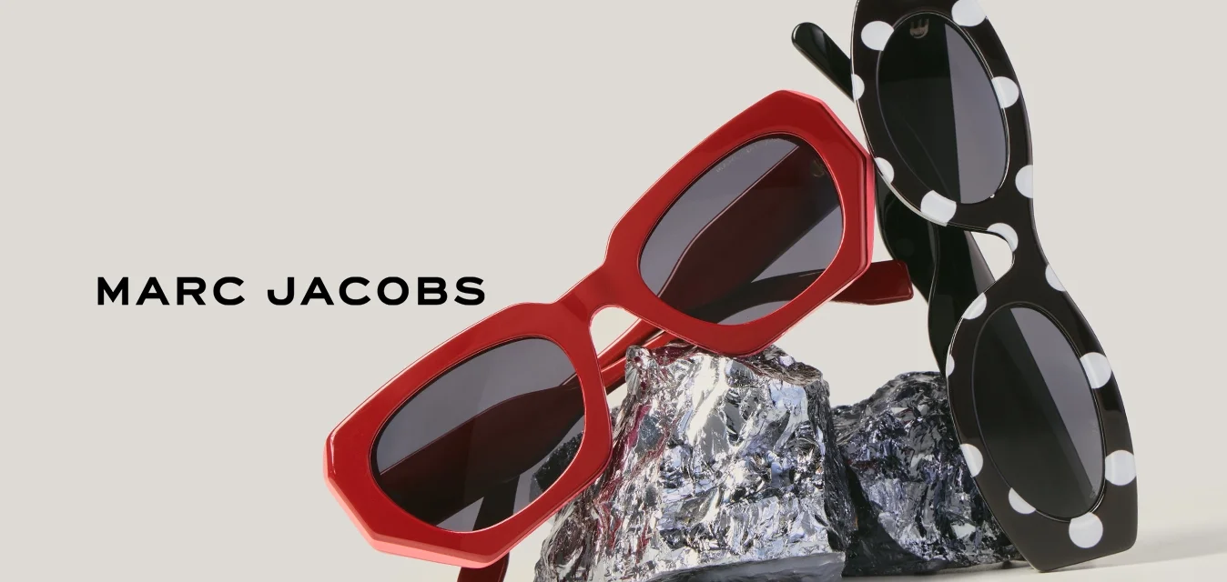 Due paia di occhiali da sole, uno rosso e uno nero con pois bianchi, appoggiati su una pellicola di alluminio stropicciata su uno sfondo semplice.