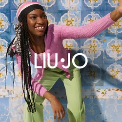 Cardigan a coste rosa, top rosa chiaro e pantaloni verdi con una texture liscia. Sullo sfondo, piastrelle blu con motivi floreali in giallo e bianco.