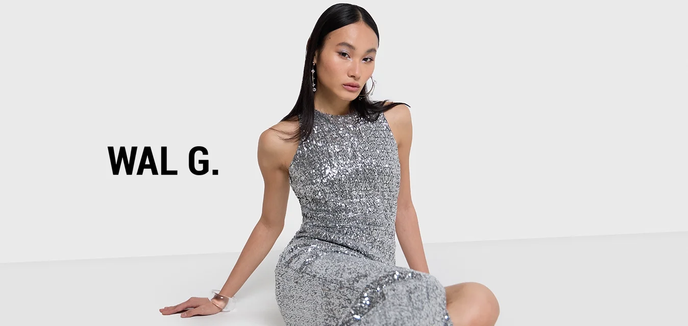 Abito da sera argento con paillettes, colletto alto e spacco. Modella che indossa tacchi alti neri e accessori. Texture liscia e lucida.