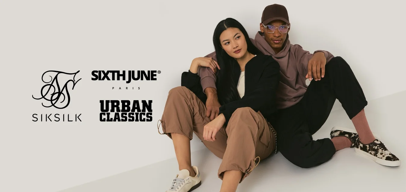 Un uomo e una donna seduti per terra, appoggiati l'uno contro l'altro, vestiti con abbigliamento casual nei toni neutri e con scarpe da ginnastica.