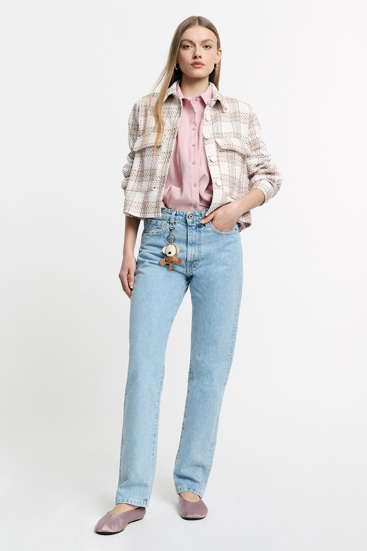 Young woman in checked cropped jacket, pink blouse and light-blue straight jeans with keyring charm, mauve flats