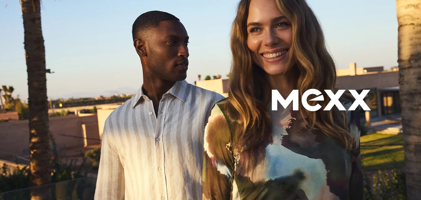 Due modelli si trovano all'aperto, uno con una camicia a righe chiara e l'altro in un vestito aderente con un motivo astratto colorato. Sullo sfondo ci sono palme.