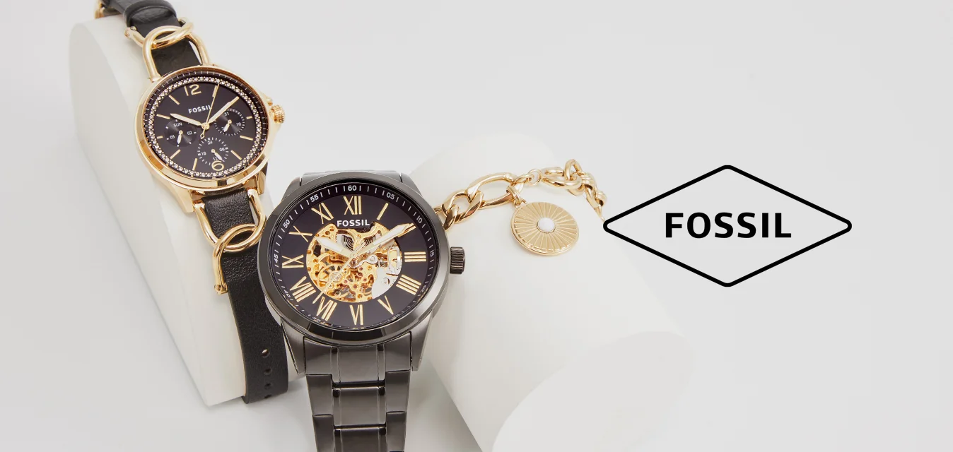 Due orologi Fossil esposti su un supporto bianco. A sinistra: oro con quadrante nero, cinturino in pelle. A destra: cassa in metallo nero, movimento visibile, dettagli dorati.