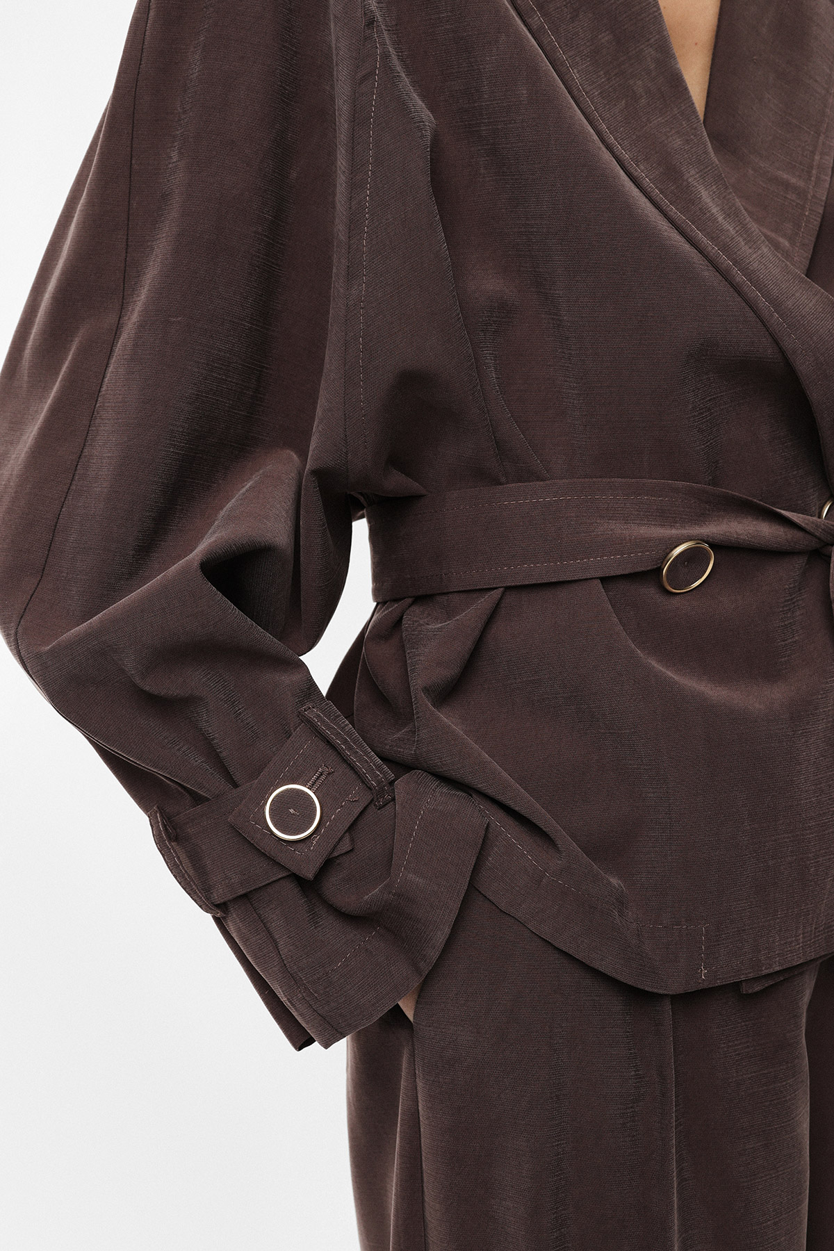 Close-up of brown textured tailored jacket with belted waist, gold ring hardware and voluminous cuff