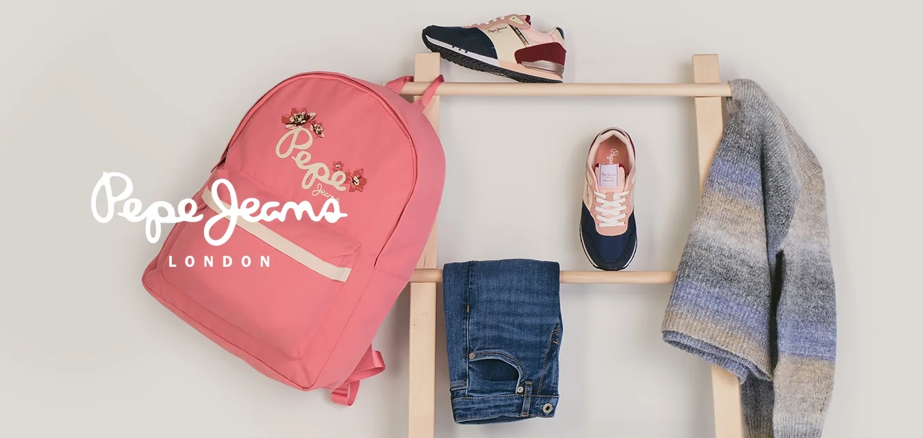 Scala di legno con uno zaino rosa, jeans blu, felpa blu navy, maglione grigio a righe e due paia di scarpe da ginnastica appoggiati contro una parete bianca.