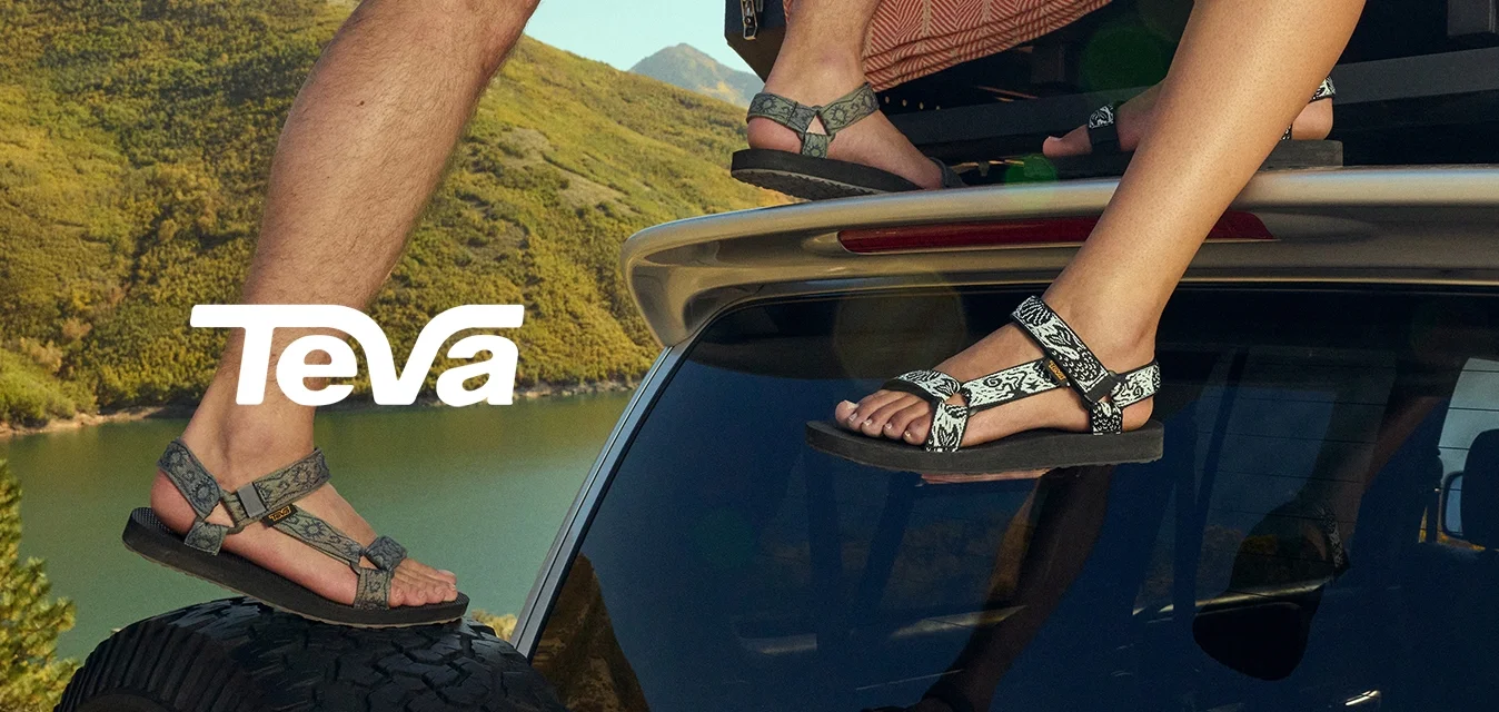 Due paia di sandali con cinturini a fantasia, uno grigio e uno nero. Entrambi hanno una suola piatta, fissati con fibbie regolabili, su un tetto di auto.