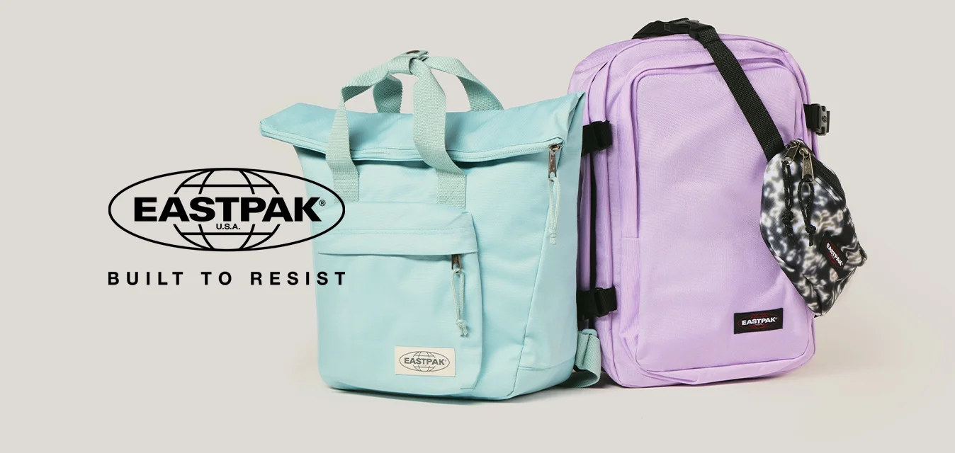 Due zaini Eastpak affiancati, uno blu chiaro con maniglie, l'altro lavanda con tracolla nera e una pochette a fantasia attaccata, su uno sfondo neutro.