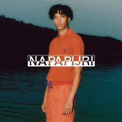 Polo arancione a maniche corte con un piccolo dettaglio della bandiera, abbinato a pantaloni corti arancioni coordinati con coulisse. Acqua sullo sfondo.