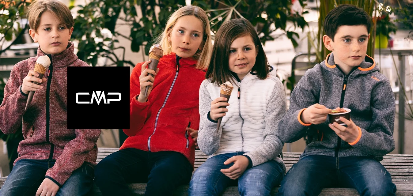 Quattro bambini siedono su una panchina di legno, tenendo coni di gelato. Indossano giacche: un pile rosso, una giacca trapuntata bianca e due giacche grigie con zip.