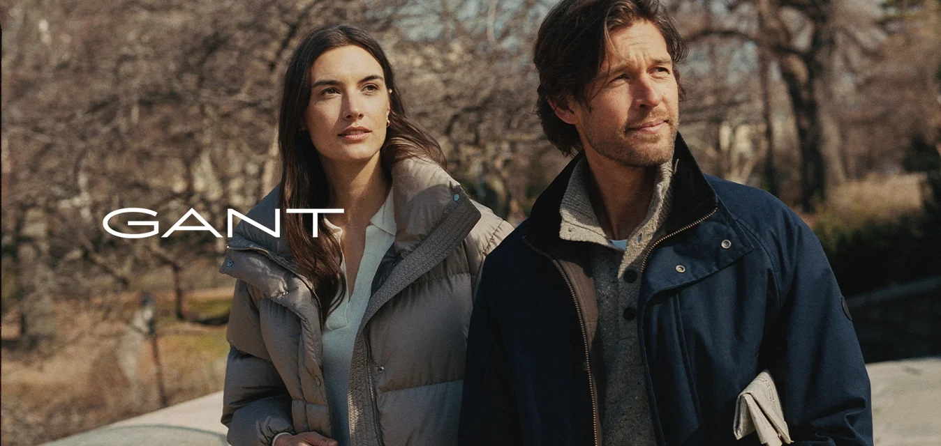 Giacca a piumino grigio chiaro con colletto alto, abbinata a un top color crema e una giacca esterna blu navy con un maglione strutturato sotto.