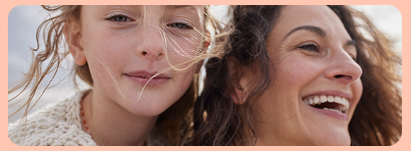 Primo piano di una donna e una bambina che sorridono all&rsquo;aperto, con capelli mossi dal vento. Immagine lifestyle senza testo sovrapposto.