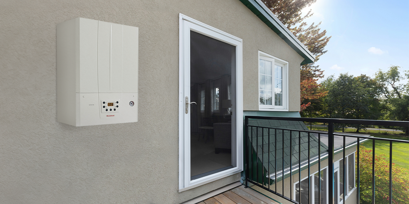 Wall-mounted domestic gas boiler installed on exterior wall beside balcony door of suburban house