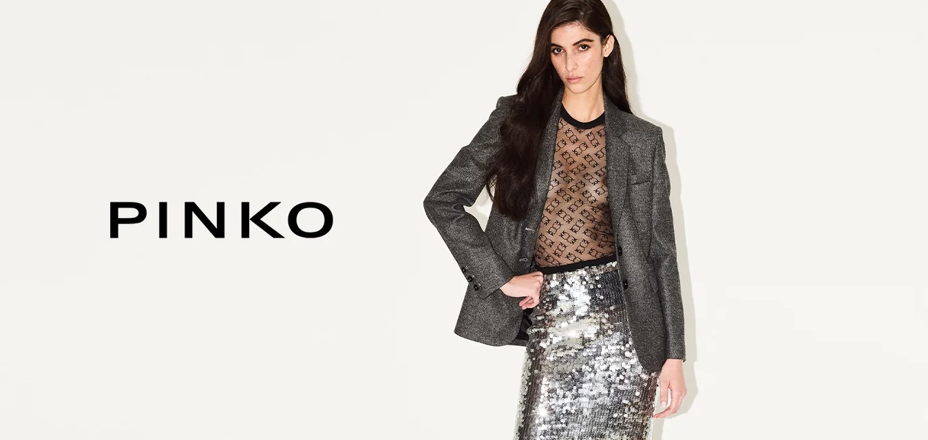 Blazer grigio su top in rete nera, gonna argentata con paillettes, collant neri e sandali con cinturino. L'outfit presenta una silhouette elegante e texture riflettenti.