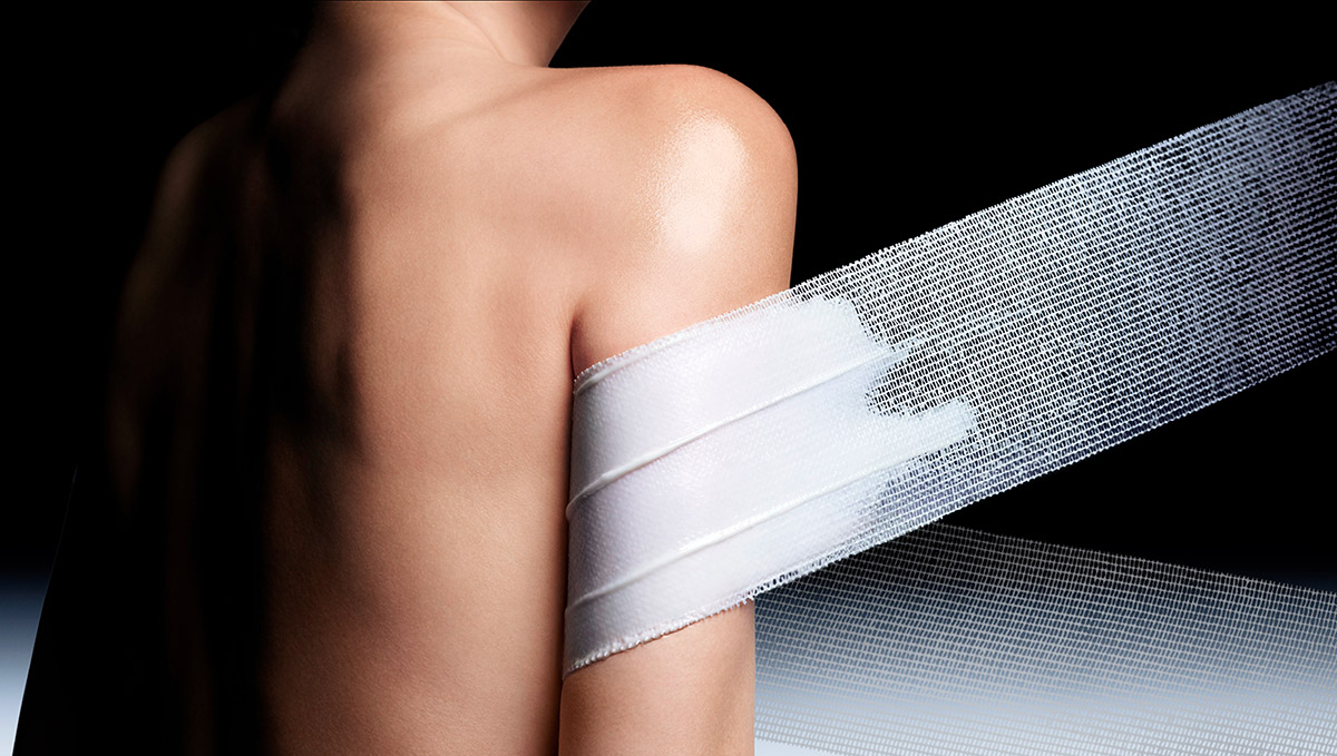 Zoom sulla schiena e sul braccio della modella la cui pelle &egrave; avvolta in una benda bianca strutturata. Questa immagine dimostra l'effetto rimodellante immediato e la sensorialit&agrave; della nuova crema corpo Replasty.