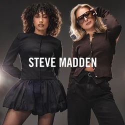 Due donne in posa con sicurezza in uno studio, una in un vestito nero con stivali, l'altra in pantaloni scuri, maglione e occhiali da sole, con luci dietro.