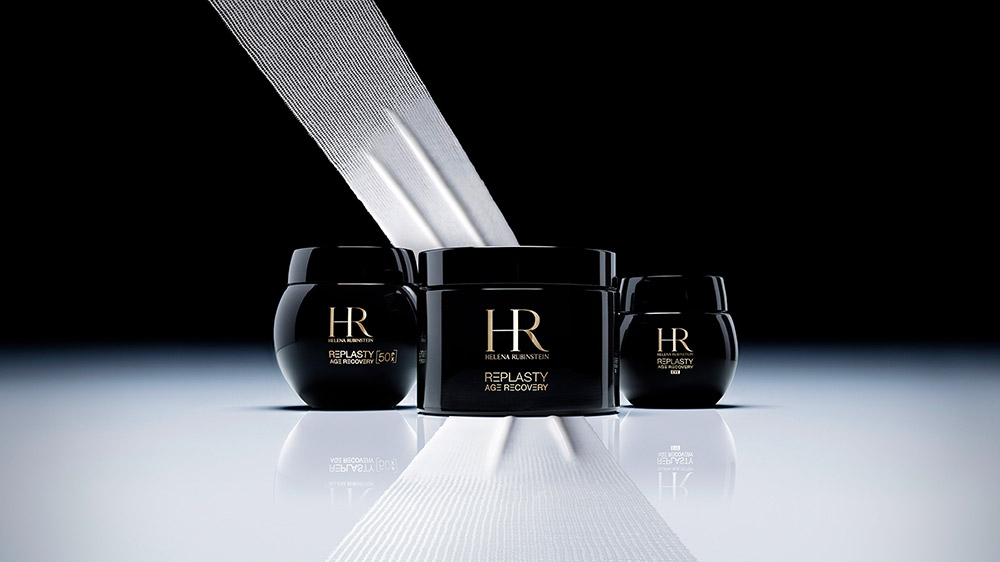 Presentazione dell'iconica linea di creme Replasty Age Recovery di Helena Rubinstein. I vasetti neri poggiano elegantemente su una texture che ricorda una benda bianca riparatrice, riflettendo l'esperienza clinica del marchio.