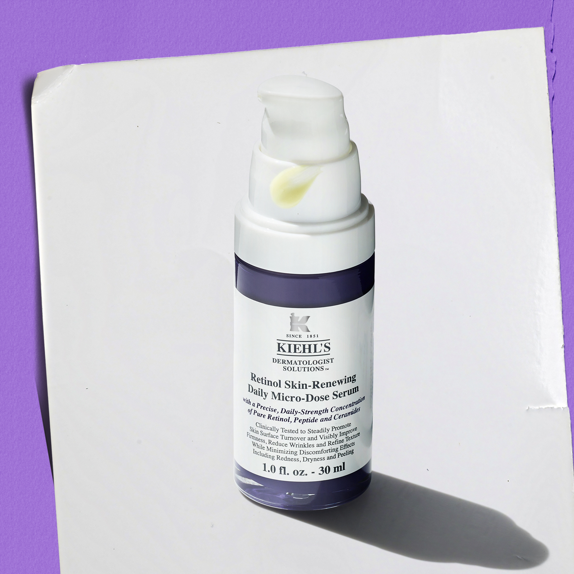 Flacone con erogatore di Retinol Skin-Renewing Daily Micro-Dose Serum Kiehl&rsquo;s da 30 ml su superficie bianca, con liquido giallo visibile sull&rsquo;erogatore. Sfondo bianco con luce viola laterale e ombra netta.