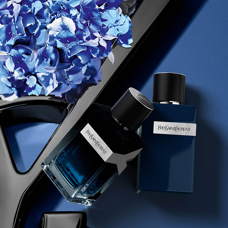 Due flaconi di profumo YSL Y su sfondo blu con delicati fiori blu.