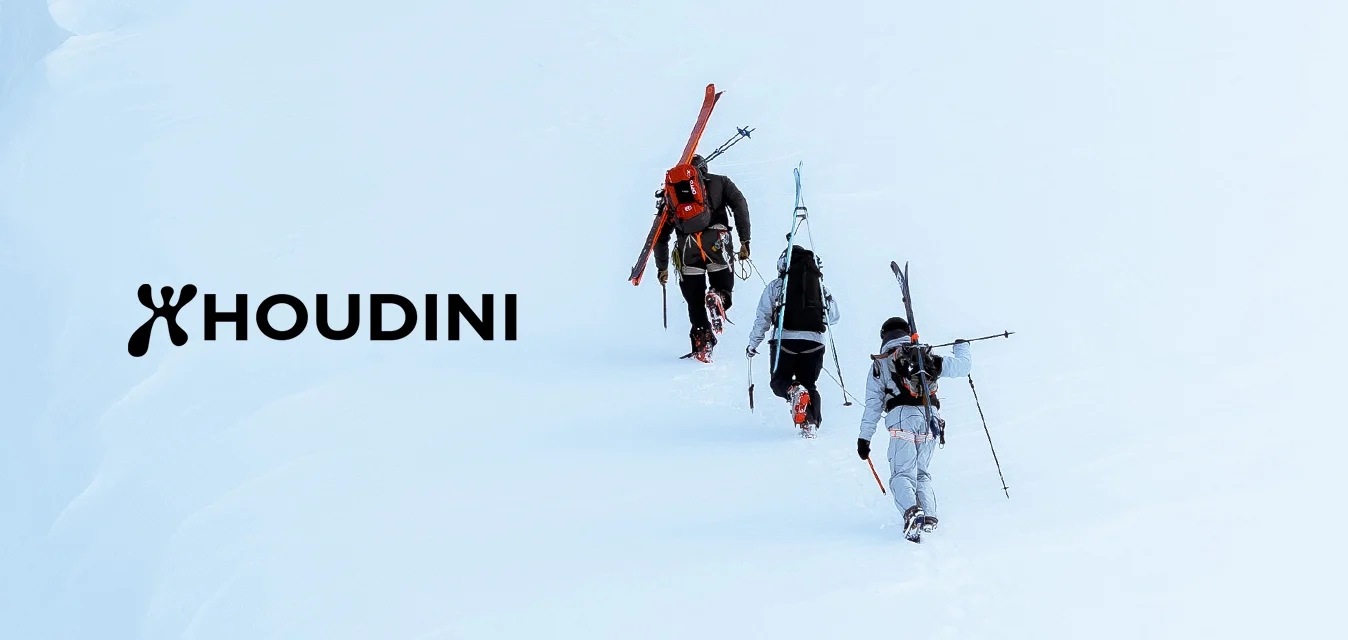 Tre sciatori con gli sci in spalla camminano in fila indiana su una ripida pendenza innevata vicino a una grande crepa di ghiaccio.