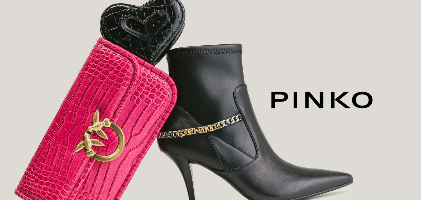 Stivaletto alla caviglia con tacco alto in pelle nera, decorato con catena dorata, accanto a una pochette rosa testurizzata con logo dorato e piccolo portamonete nero a forma di cuore all'interno.