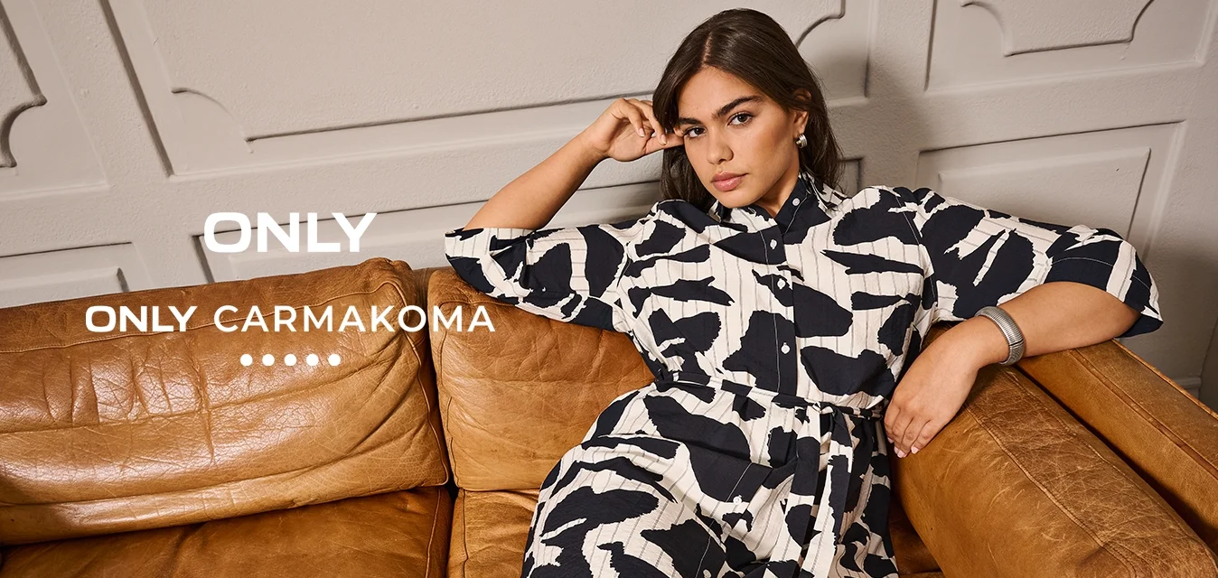 Donna con capelli scuri rilassata su un divano in pelle marrone, indossa un vestito nero con motivo bianco a maniche tre quarti, poggiando il braccio sul bracciolo.