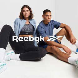 Due persone sono sedute su un pavimento bianco. Una indossa una giacca azzurro chiaro, leggings neri e sneakers bianche. L'altra indossa una maglietta blu e pantaloni corti.