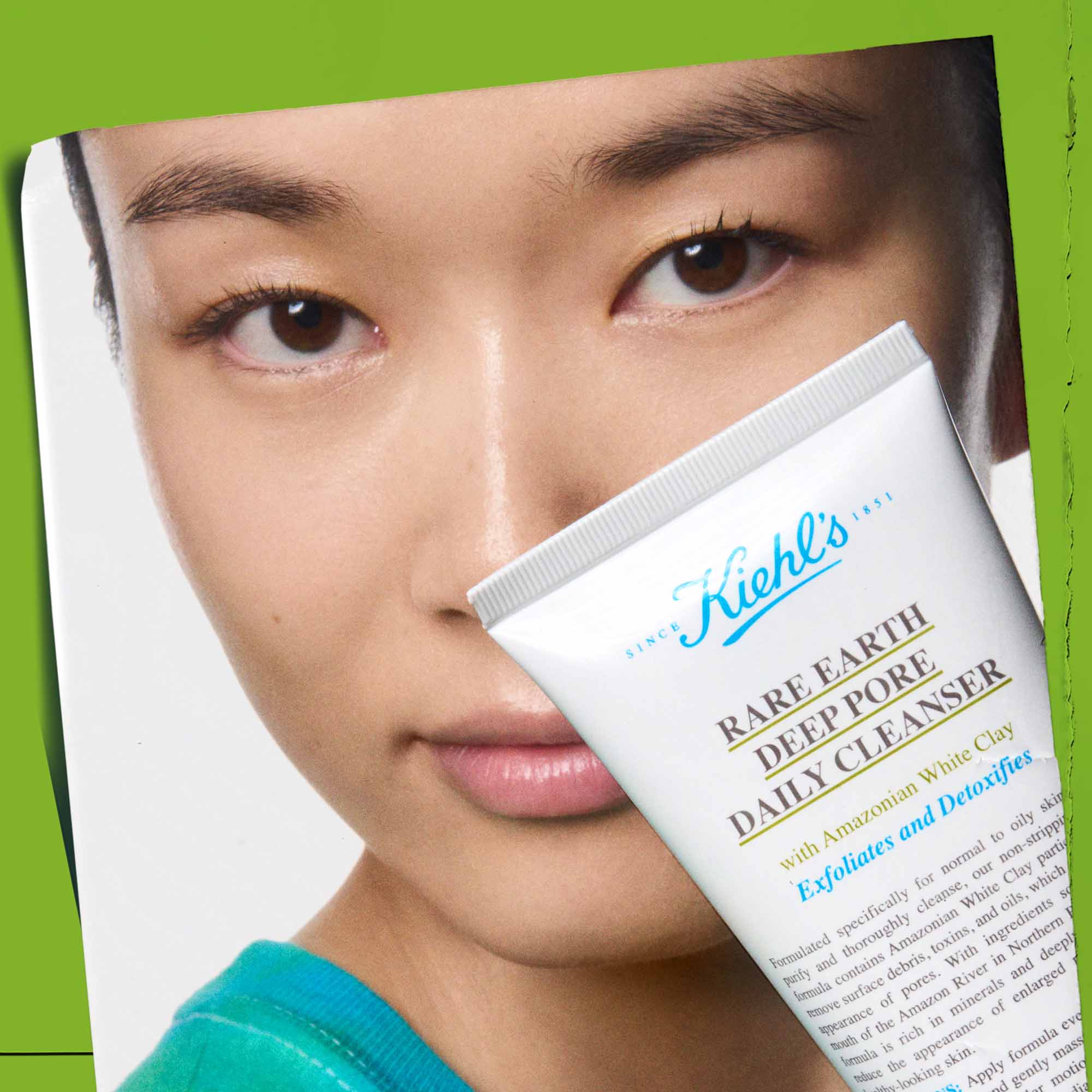 Primo piano di Facial Fuel Energizing Scrub Kiehl&rsquo;s in tubo blu da 100ml, tenuto sopra la fronte di un modello uomo. Prodotto esfoliante energizzante per pelle maschile.