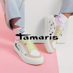 Persona che indossa jeans di denim chiaro, sneakers bianche con lacci verde pastello e disegni in stile scritto a mano, e calzini bianchi con testo rosso.