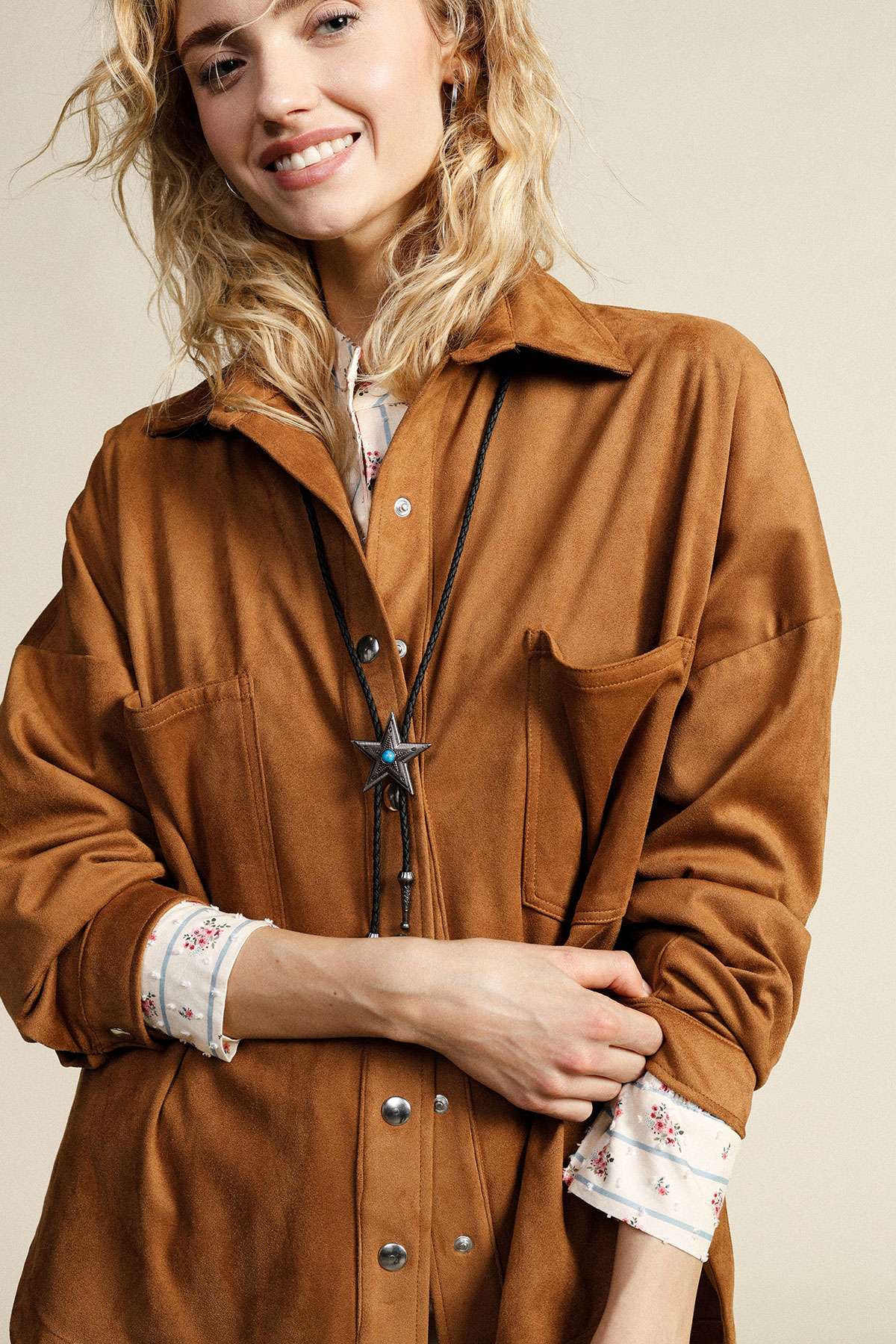 Smiling woman wearing brown suede jacket with star bolo tie and floral shirt cuffs visible
