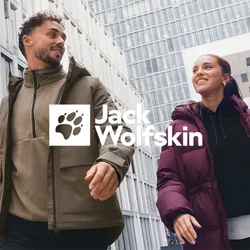 Due persone con giacche invernali camminano e sorridono all'aperto davanti a moderni uffici in un contesto urbano in una giornata nuvolosa.