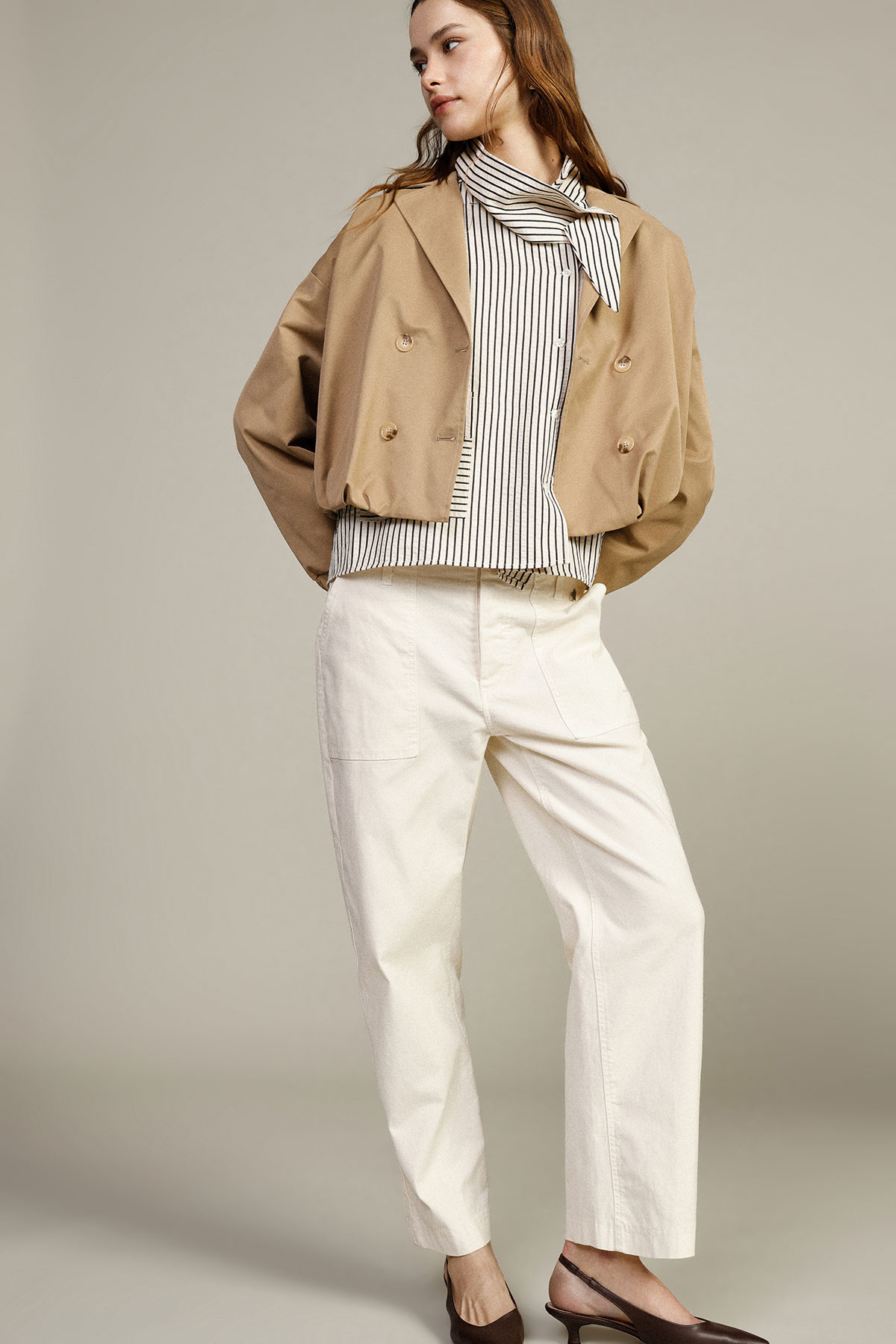 Woman modelling cropped tan double-breasted jacket, striped tie-neck blouse, cream wide-leg trousers and brown slingback shoes