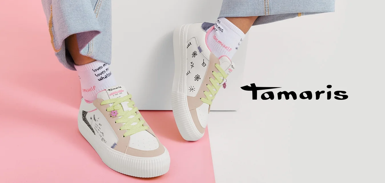 Persona che indossa jeans di denim chiaro, sneakers bianche con lacci verde pastello e disegni in stile scritto a mano, e calzini bianchi con testo rosso.