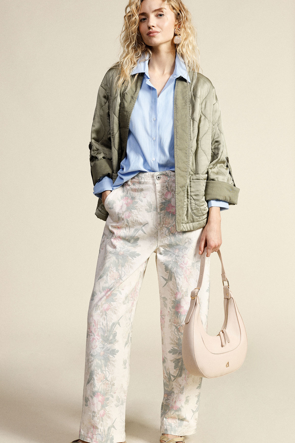Model wearing light blue shirt, khaki quilted jacket, floral wide‑leg trousers and pale pink shoulder bag, hands in pockets
