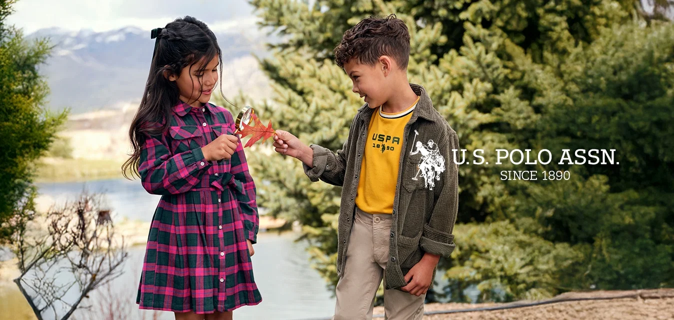 Bambini che giocano all'aperto; ragazza in un vestito scozzese con vita accentuata e stivali marroni; ragazzo in una camicia gialla e giacca di velluto a coste verde con pantaloni beige.