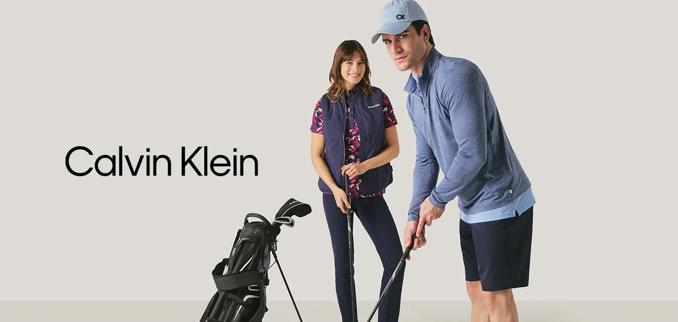 Uomo e donna che si preparano a giocare a golf al chiuso con mazze da golf e una sacca da golf su uno sfondo neutro.