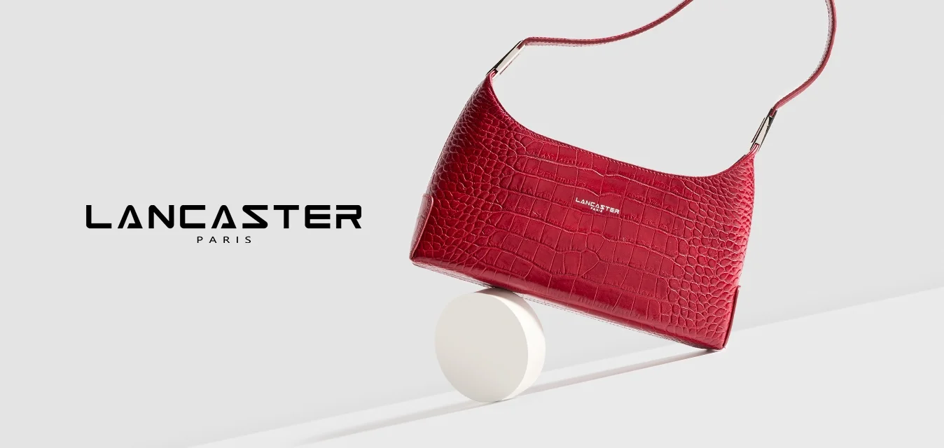 Borsa a mano in pelle sintetica rossa effetto coccodrillo con forma curvata, tracolla regolabile e dettagli in metallo argentato, posata su un pedistallo circolare bianco.