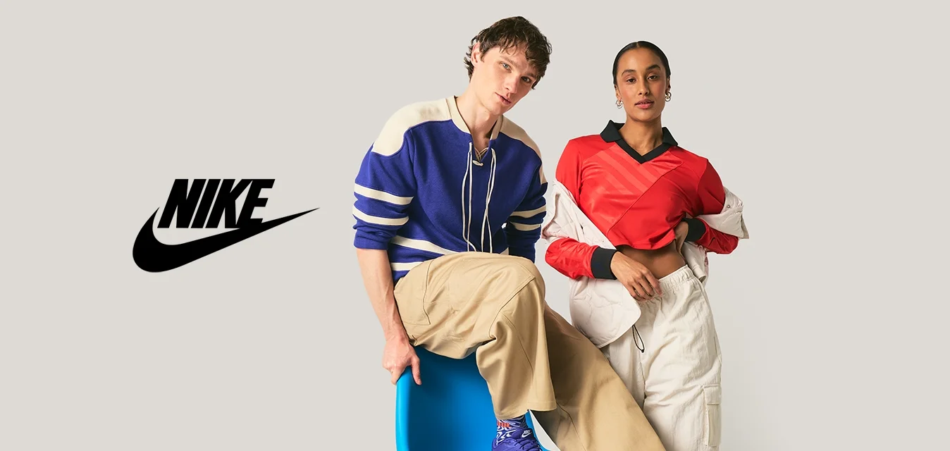 Due giovani adulti in abiti casual posano; uno è seduto su una sedia moderna blu, l'altro sta in piedi con una mano in tasca contro uno sfondo semplice.